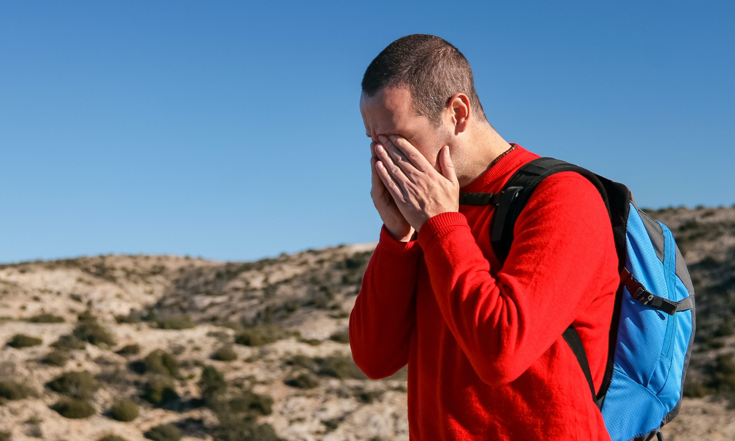 man wearing red crew-neck man wearing red crew-neck sweater with teal and black backpack outdoor during daytime