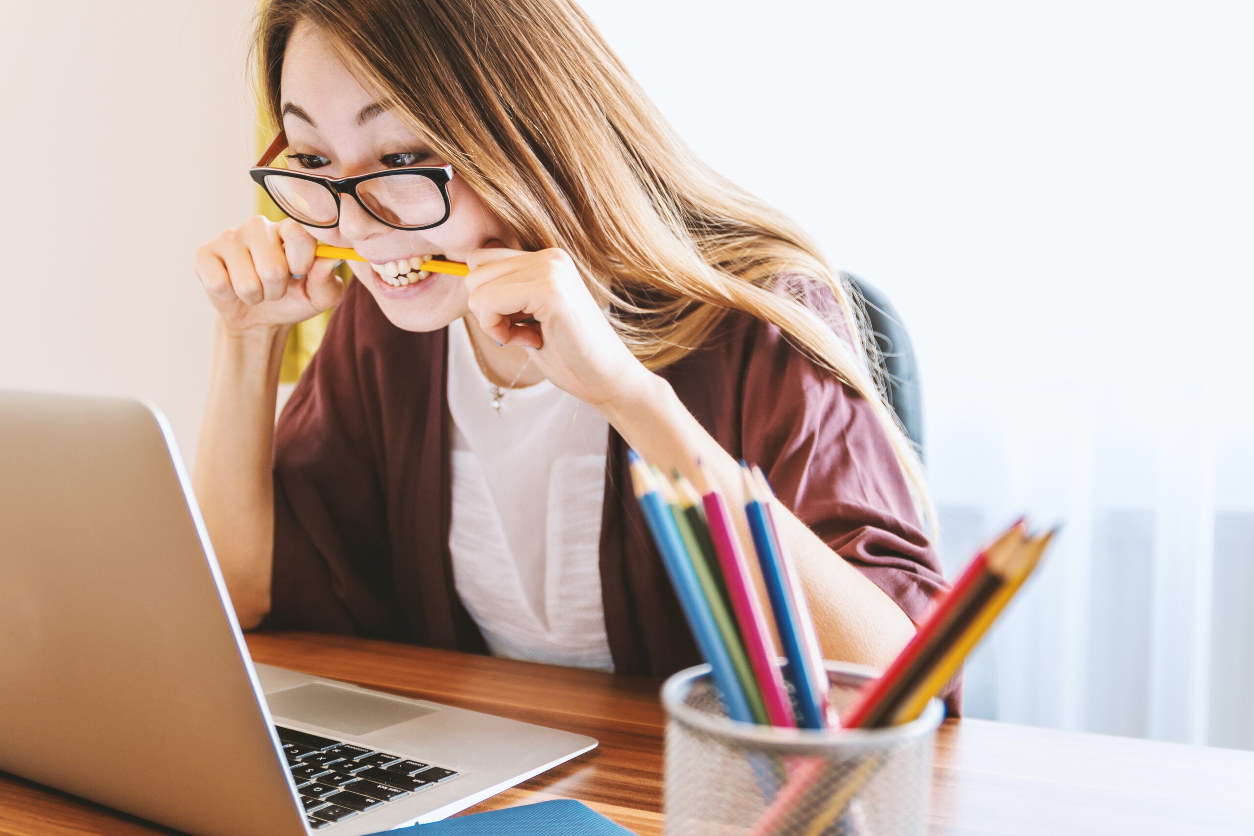 woman biting pencil while woman biting pencil while sitting on chair in front of computer during daytime