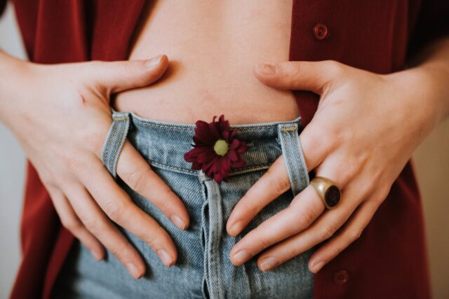 Photo by Anete Lusina Crop faceless female in casual clothes decorated with blooming flower revealing bare stomach